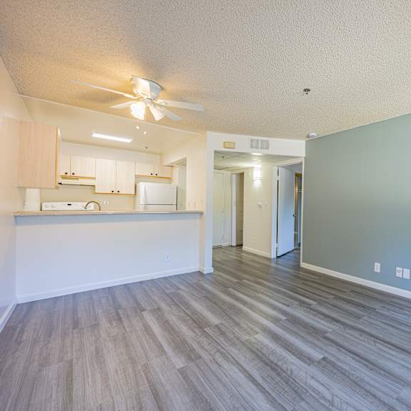 a room with a ceiling fan and a kitchen area in the background.