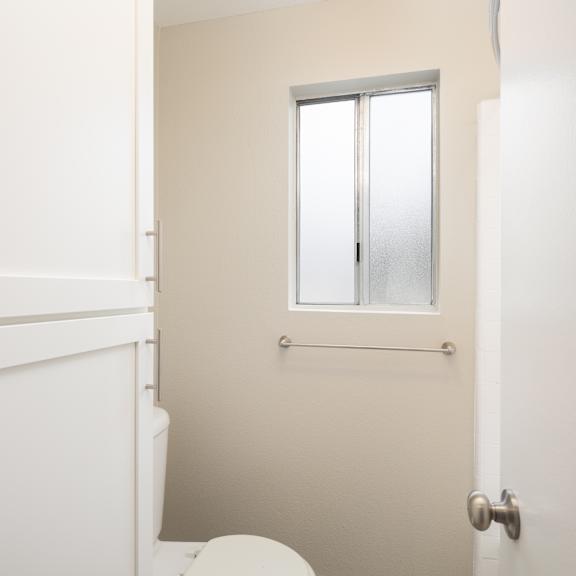 a white toilet sits in a bathroom with a door and a window.