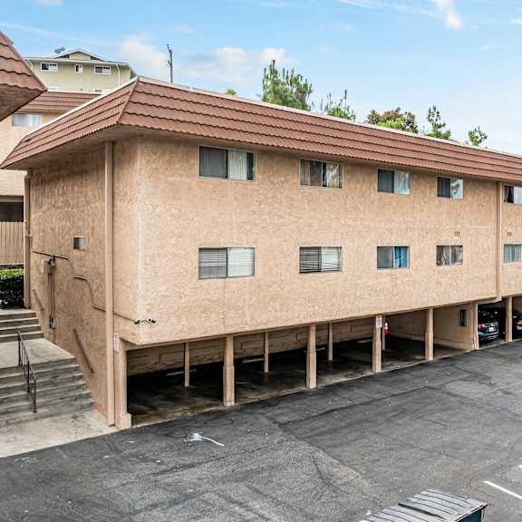 a parking lot in front of a tan building with a brown roof.