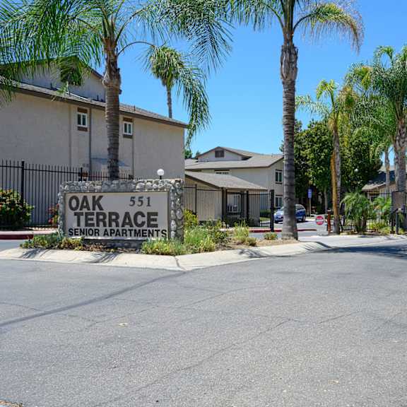 a street with houses on each side and a sign that reads oak 51 terrace at oak terrace senior apts, hemet california