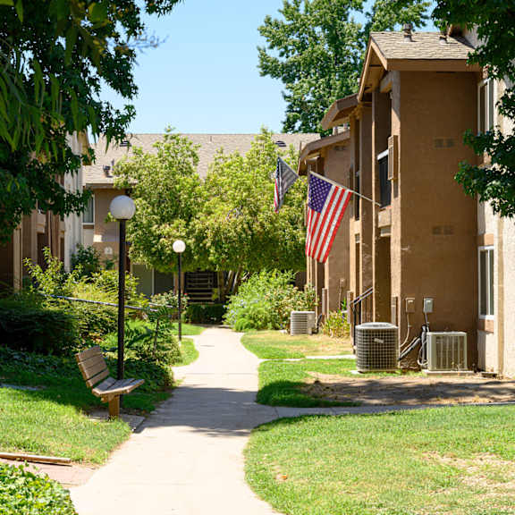 a pathway lined with green grass and trees in front of an apartment building at oak terrace senior apts, hemet
