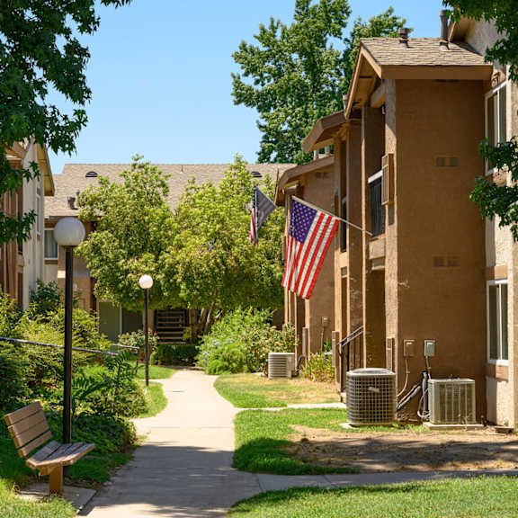 a pathway with a bench and trash cans in front of an apartment building at oak terrace senior apts, california, 92543