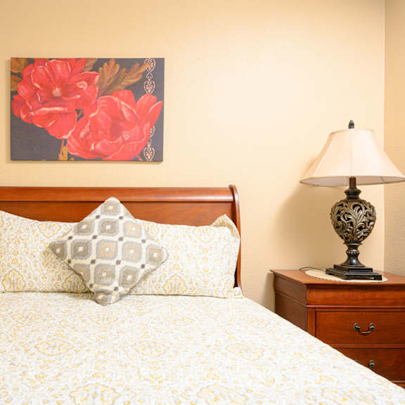 a bedroom with a bed and a nightstand with a lamp at oak terrace senior apts, hemet, ca 92543