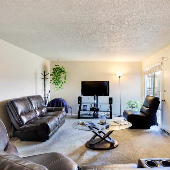 a living room with a black leather couch, a black chair, a black coffee table, and a flat screen tv.