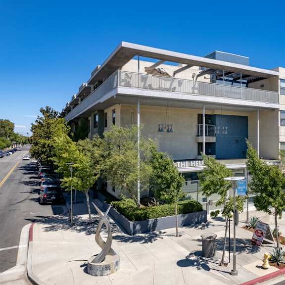 an apartment building with a parking lot and trees in front of it at helix at university village, pomona, ca