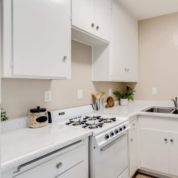 a kitchen with white cabinets and a stove and sink at university park, azusa, ca