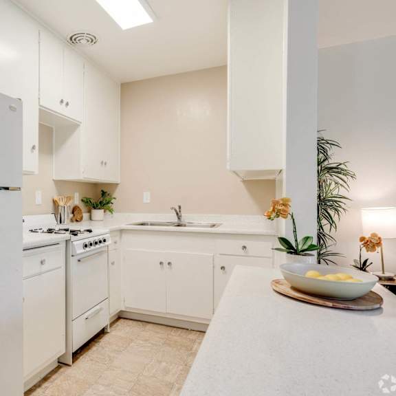 a white kitchen with white cabinets and a white refrigerator at university park, azusa, ca 91702