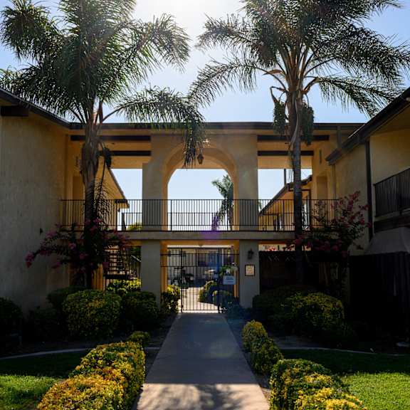 a walkway between two buildings with palm trees in the middle of the walkway at park columbia apts, hemet, 92544