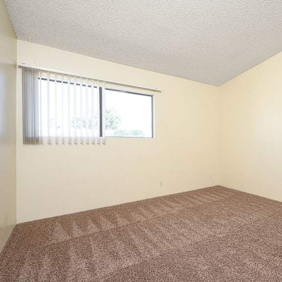 a bedroom with white walls and a window at park columbia apts, hemet, ca 92544