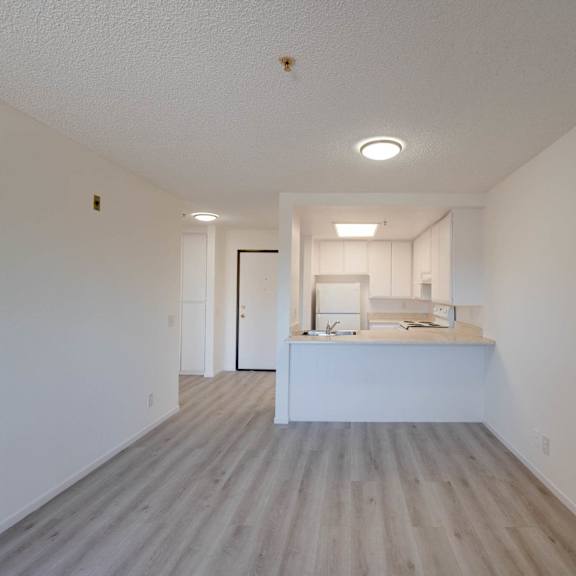an empty living room and kitchen with white walls and wood floors at flamingo garden senior apts, el monte