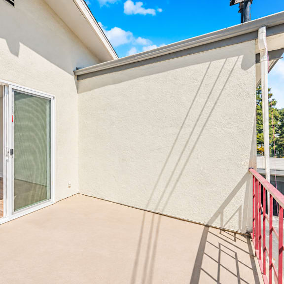 a balcony with a red railing and a sliding glass door leading to an empty room.