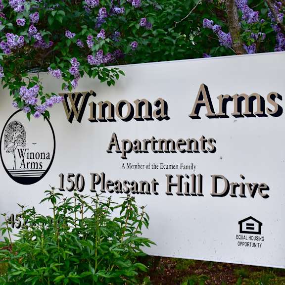 a sign for winona arms apartments is displayed in front of some purple flowers.