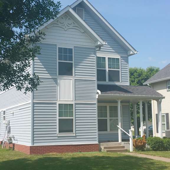 a white house with a porch and a red brick base.