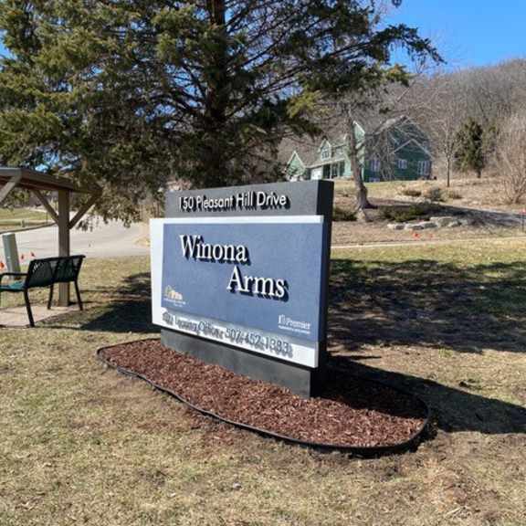 a sign for winona arms is displayed in front of a tree.