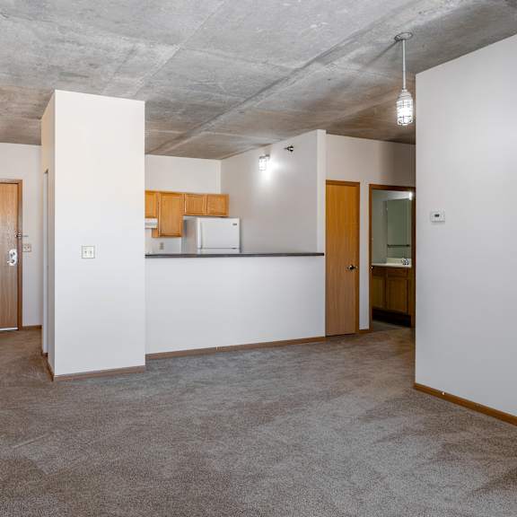 a spacious, empty room with a kitchen area in the background.
