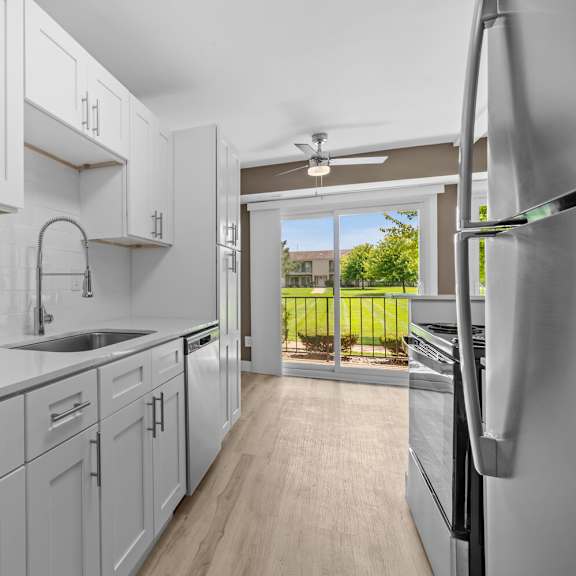 a white kitchen with white cabinets and a sliding glass door at sunnymede apartments - troy, mi, troy