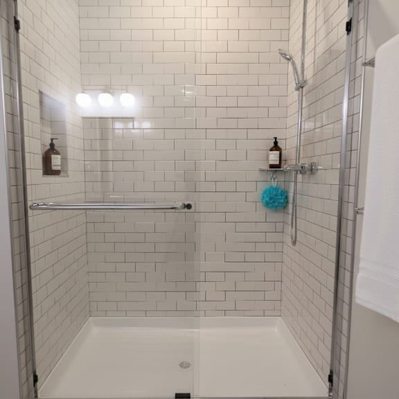 a white tiled shower with a white tub and a white towel hanging on the door.