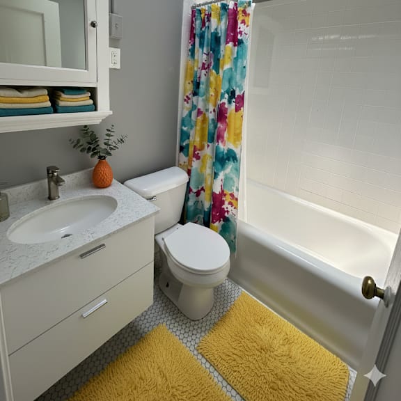 a bathroom with a yellow rug in front of a white toilet and a shower curtain.