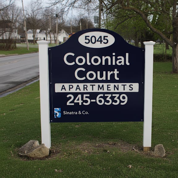 a sign for colonial court apartments is displayed in front of a tree.