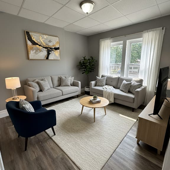a living room with a grey couch, a blue armchair, a wooden coffee table, and a painting on the wall.