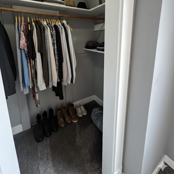 a small closet with clothes hanging and shoes on the floor.
