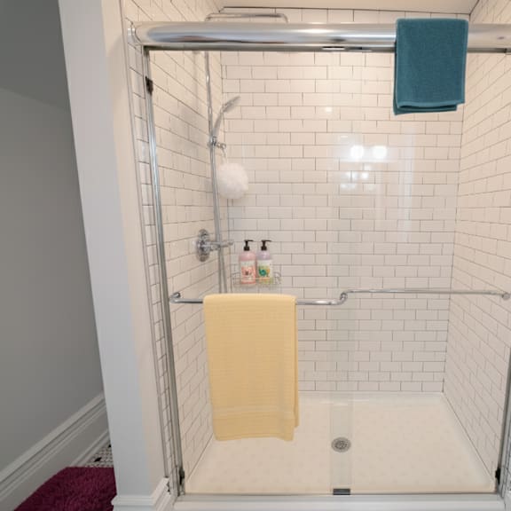 a white tiled shower with a yellow towel hanging on the railing.