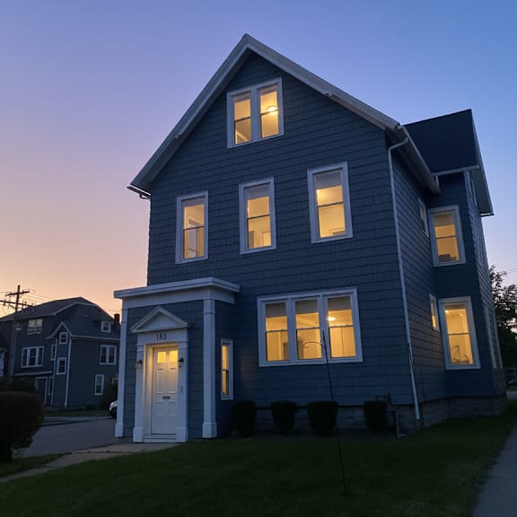 a blue house with a white door and windows is illuminated from the inside.