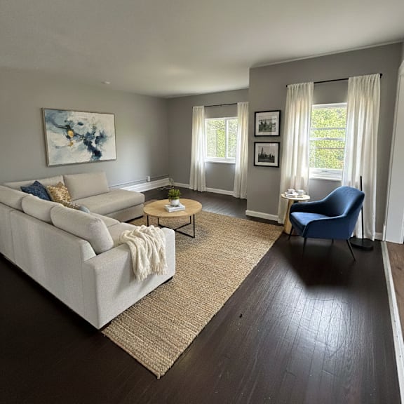 a living room with a white couch, a blue chair, and a painting on the wall.