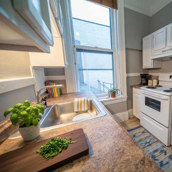 a kitchen with a white refrigerator and a wooden cutting board with green herbs on it.