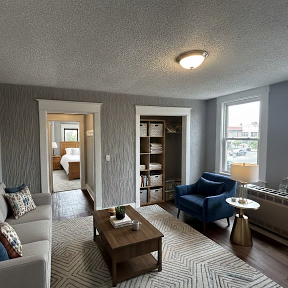a living room with a grey couch, a blue chair, a coffee table, and a painting on the wall.