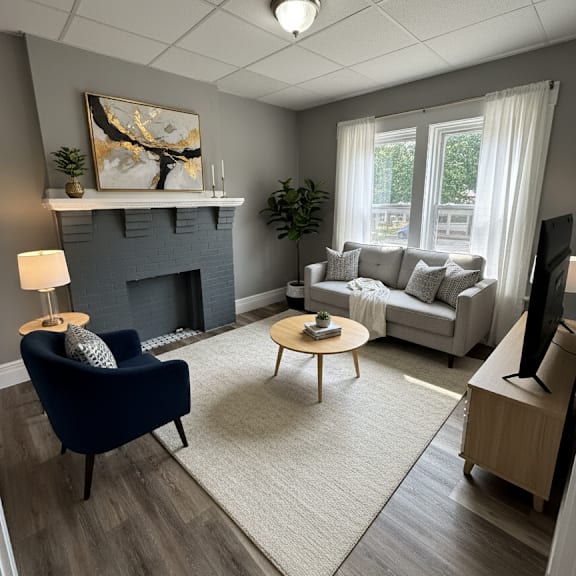 a living room with a blue armchair, a grey couch, a fireplace, and a painting on the wall.