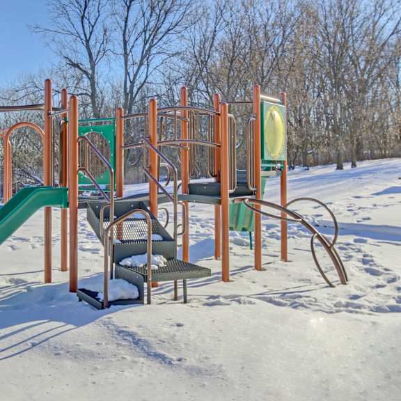 a playground with a green slide and orange structure in the snow.