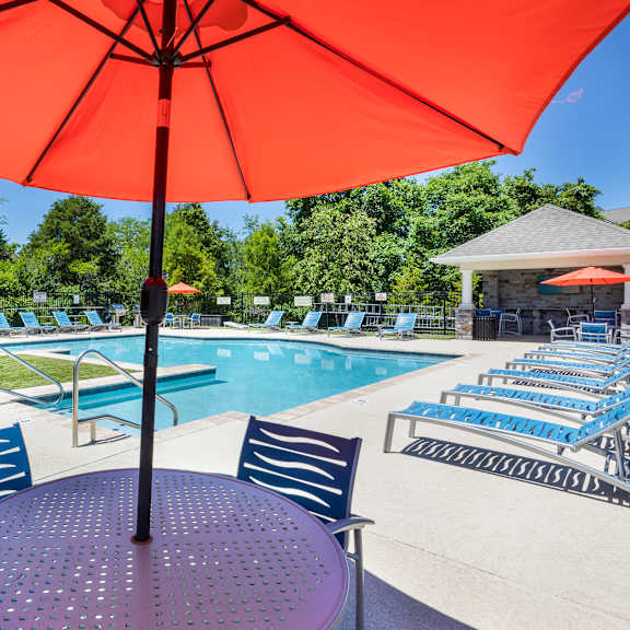 our apartments have a pool and patio with chairs and an umbrella at aventura at towne centre, missouri, 63011