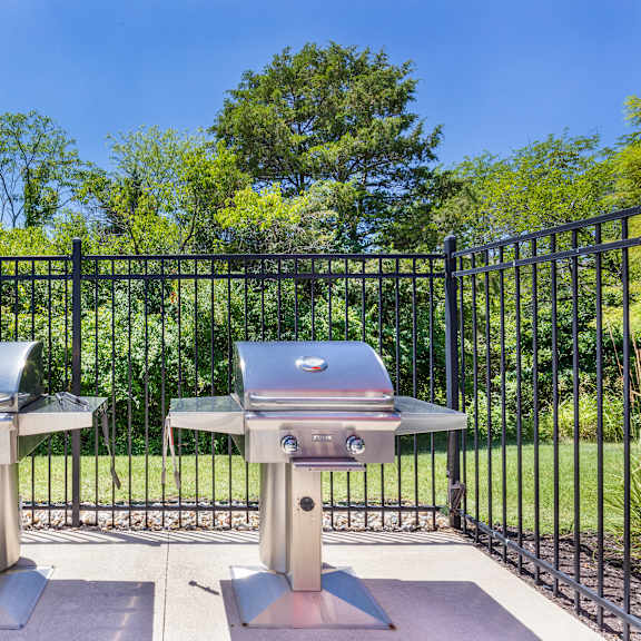 two bbqs in front of a fence with trees at aventura at towne centre, ellisville, missouri