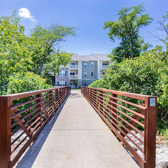 a bridge with a building in the background and trees at aventura at towne centre, missouri, 63011