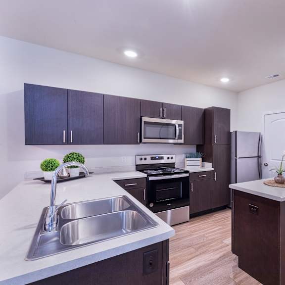 a kitchen with white counter tops and dark cabinets and stainless steel appliances at aventura at towne centre, missouri