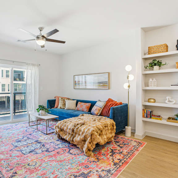 Thumbnail 3 of 37 A living room with a blue couch and a colorful rug. at ThreeTwenty at the Vybe Apartments, Texas, 78640