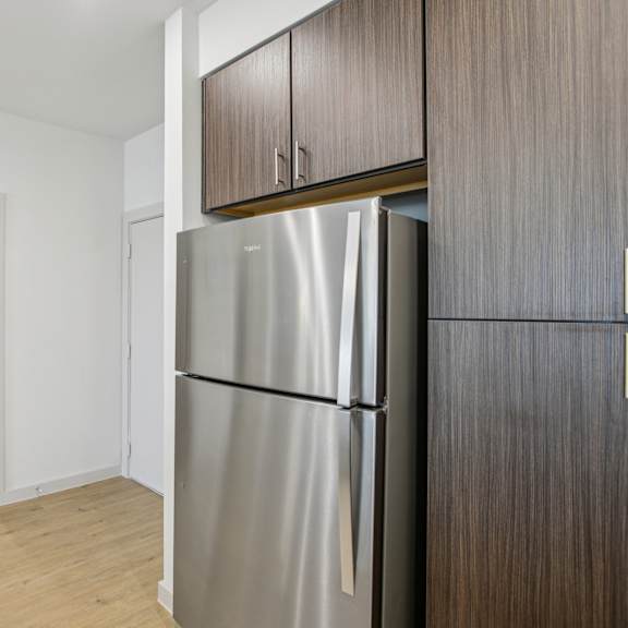 Thumbnail 13 of 37 A kitchen with a refrigerator and wooden cabinets. at ThreeTwenty at the Vybe Apartments, Kyle, TX, 78640