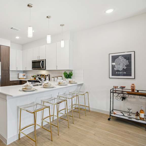 Thumbnail 14 of 37 A modern kitchen with a white island and gold bar stools. at ThreeTwenty at the Vybe Apartments, Kyle, 78640
