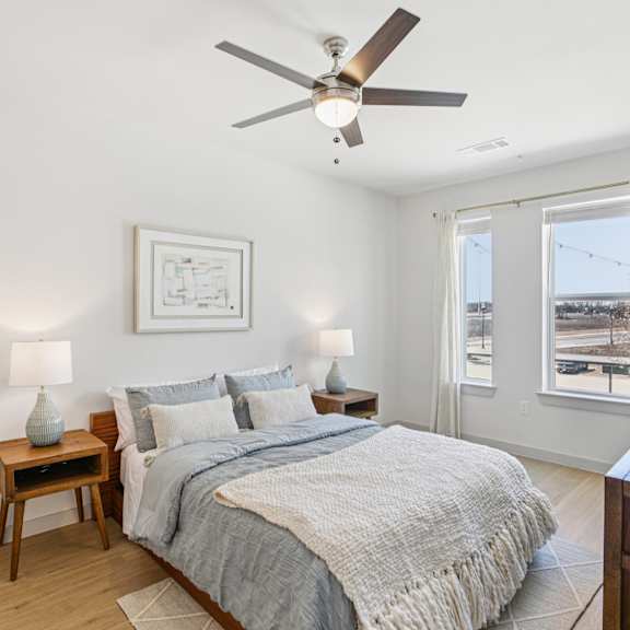 Thumbnail 17 of 37 A bedroom with a bed, a ceiling fan, and a plant at ThreeTwenty at the Vybe Apartments, Kyle