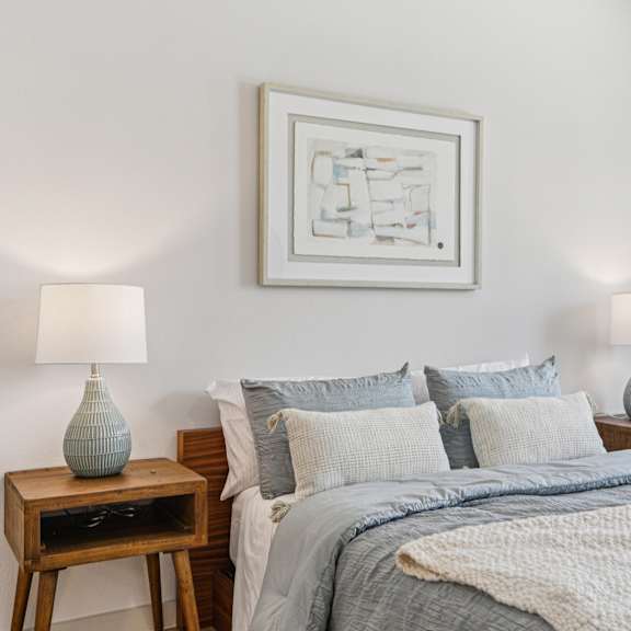 Thumbnail 18 of 37 A bedroom with a bed, two lamps, and a painting on the wall at ThreeTwenty at the Vybe Apartments, Kyle, TX