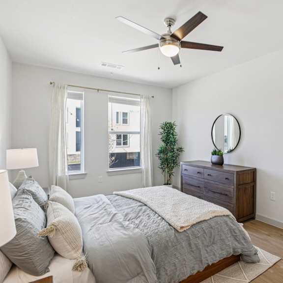 Thumbnail 20 of 37 A bedroom with a bed, dresser, mirror, and a ceiling fan. at ThreeTwenty at the Vybe Apartments, Kyle