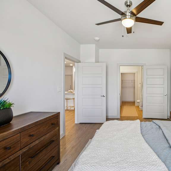 Thumbnail 22 of 37 A bedroom with a bed, dresser, and mirror at ThreeTwenty at the Vybe Apartments, Texas