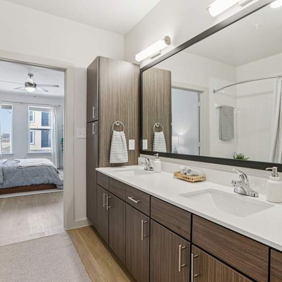 Thumbnail 30 of 37 A bathroom with a large mirror and a bedroom with a bed and a window. at ThreeTwenty at the Vybe Apartments, Kyle, Texas