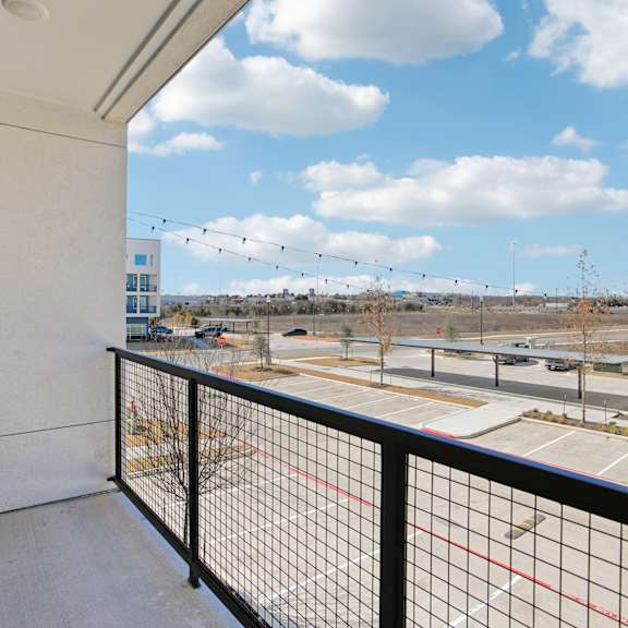 Thumbnail 36 of 37 A balcony with a black railing overlooks a parking lot and buildings at ThreeTwenty at the Vybe Apartments, Texas, 78640