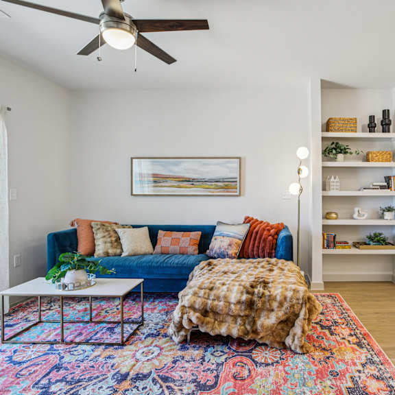 Thumbnail 6 of 37 A living room with a blue couch and a colorful rug at ThreeTwenty at the Vybe Apartments, Kyle, TX, 78640