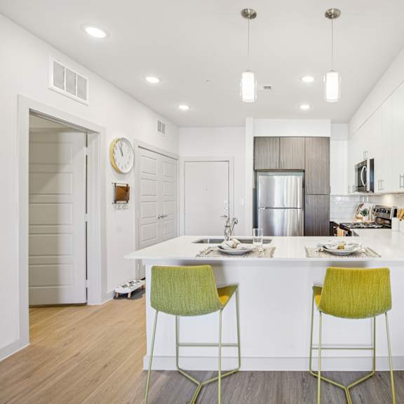 Thumbnail 9 of 23 A kitchen with a white counter and two green chairs at ThreeTwenty at the Vybe Apartments, Kyle, TX