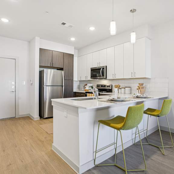 Thumbnail 10 of 23 A kitchen with a white island and yellow chairs at ThreeTwenty at the Vybe Apartments, Kyle, 78640