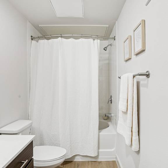 Thumbnail 16 of 23 A white bathroom with a toilet, sink, and shower at ThreeTwenty at the Vybe Apartments, Texas, 78640