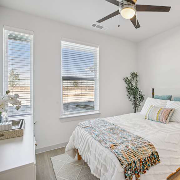 Thumbnail 17 of 23 A bedroom with a bed, a ceiling fan, and a nightstand with a lamp. at ThreeTwenty at the Vybe Apartments, Kyle, Texas